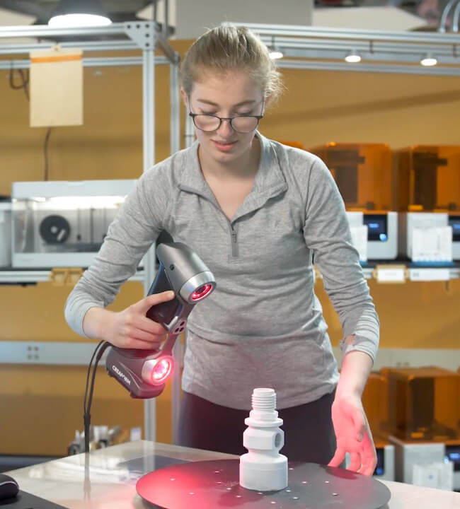 Engineer using a Creaform Go!SCAN 3D handheld scanner to capture precise measurements of a 3D-printed part in a workshop.