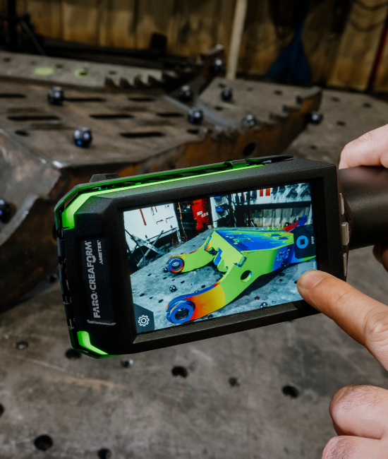 Hand holding a Creaform HandyPROBE portable probing device, inspecting an orange industrial mold for precise measurements in a quality control process.